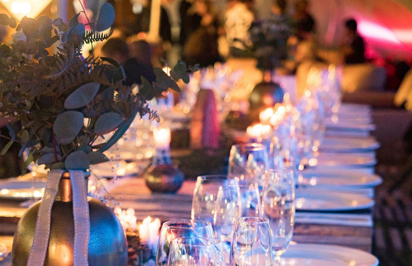 A long candlelit dinner table set for a ticketed supper club event